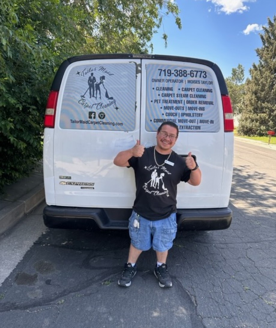 Owner of Tailor Maid Carpet Cleaning gives thumbs-up while standing in front of a white van with "Tailor Made Carpet Cleaning" signage, detailing cleaning services and contact info.